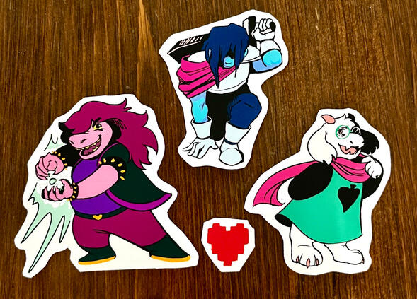 Three matte stickers of Deltarune characters. Left, Susie; Top Middle, Kris; Right, Ralsei.